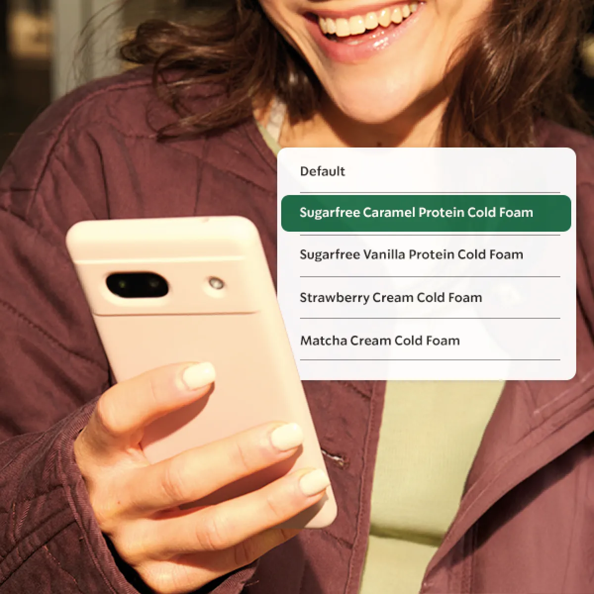 A person smiles at their phone, seeing the new protein cold foam options in the customisation list on our menu.